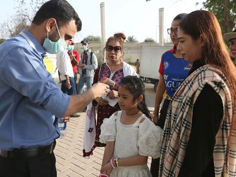 A Pakistani volunteer takes the temperature of a young spectator outside the National Stadium in Karachi, Pakistan, Thursday, March 12, 2020. 