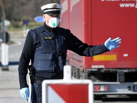 A German police officer, wearing a face mask, stops a driver at the border crossing between Austria and Germany, near the German village of Oberaudorf. 