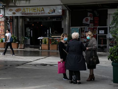 Women wearing protective masks chat at a central square, in Athens, Sunday, March 15, 2020. 
