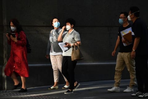 People wearing face masks, amid concerns of the COVID-19 coranavirus, walk on a street in Sydney on March 19, 2020.