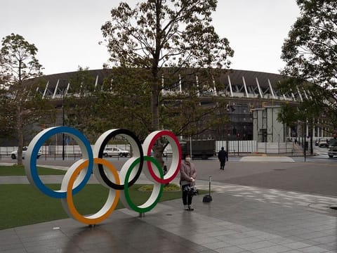 A woman pauses for photos next to the Olympic rings near the New National Stadium in Tokyo