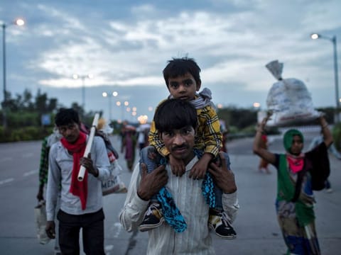 A migrant worker carries his son as they walk along a road with others to return to their village, during a 21-day nationwide lockdown to limit the spreading of coronavirus disease (COVID-19), in New Delhi on March 26, 2020. 