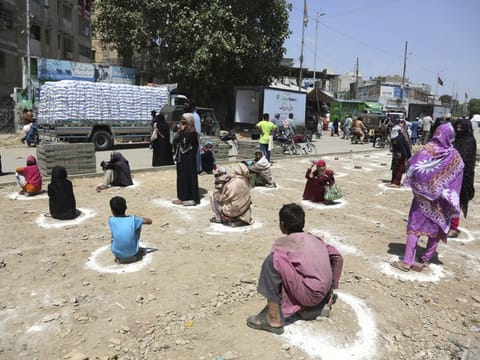People sit at distance to receive relief goods during a nation-wide lockdown to contain outbreak of the coronavirus, in Karachi on Friday.