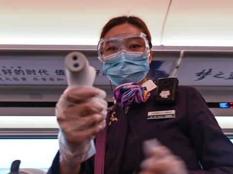 A worker wearing a face mask as a preventive measure against the COVID-19 novel coronavirus takes the temperature of train passengers, one of the stops being Wuhan, in Danyang on March 28, 2020. The Chinese city of 11 million people that was Ground Zero for what became the global coronavirus pandemic partly reopened on March 28, after more than two months of almost total isolation. 