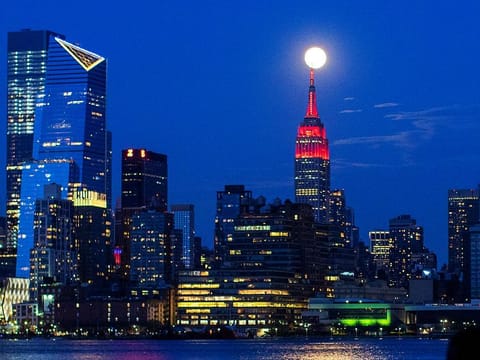 The Supermoon rises behind the Empire State Building while it glows red in solidarity with those infected with coronavirus as the outbreak of the disease (COVID-19) continues in the Manhattan borough of New York City, as it is seen from Hoboken, New Jersey, U.S., April 7, 2020.