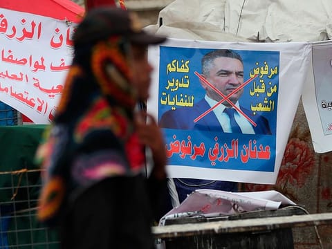 An anti-government protester passes a defaced picture of Iraq's Prime Minister-designate Adnan Al-Zurfi in Tahrir Square, Baghdad, Iraq, Wednesday, March 18, 2020. Iraq's president named Al-Zurfi as prime minister-designate, following weeks of political infighting, as Baghdad residents rushed to stock up on supplies hours before a days-long curfew was set to take hold amid a global pandemic. 