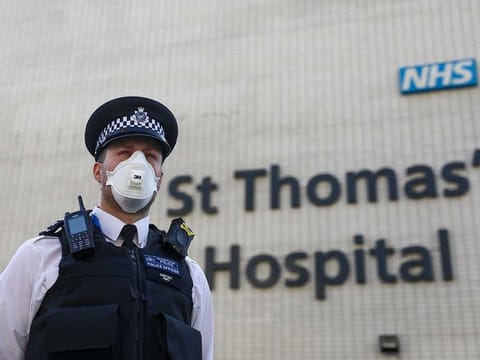 A police officer, wearing a protective face mask, stands outside St Thomas Hospital in London 