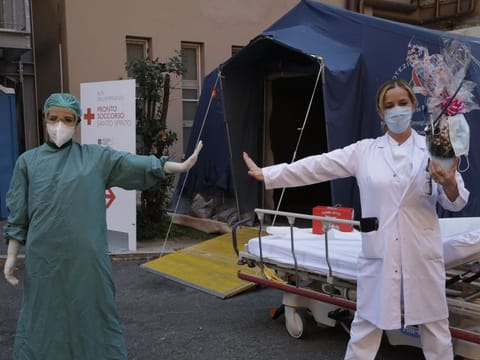 Monica Carfora, right, deputy head of the emergency of the Santo Spirito Hospital, which now has a separate emergency for possible covid patients, holds a chocolate Easter egg as she poses for a photograph with nurse Silvia Sforza, holding out their arms to indicating social distancing, outside the entrance to for COVID-19 emergency, in central Rome, Sunday. 
