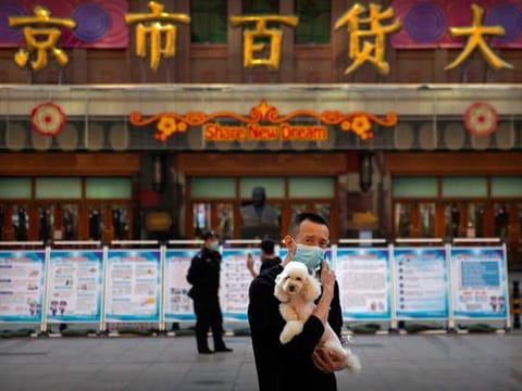 A man wearing a face mask to prevent the spread of the new coronavirus holds a dog as he stands along a pedestrian shopping street in Beijing, Tuesday, April 28, 2020. The Chinese city of Wuhan, which was the original epicentre of the pandemic, again reported no new coronavirus cases or deaths Tuesday and its hospitals remained empty of virus patients for a second straight day. 