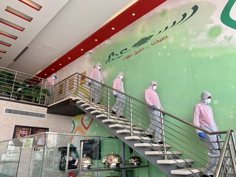 Restaurant workers wearing protective suits walk to disinfect the restaurant's cars to prepare them for food delivery. Saudi Arabia has linked salary cuts to a proportional reduction in working hours.