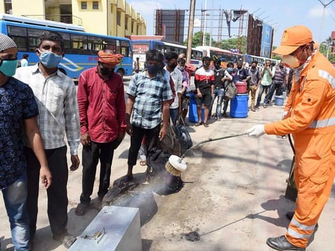 Workers disinfect the luggage of migrants as they stand in a queue to board a bus to go back home, in Patna. 