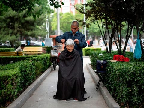 A barber cuts the hair of an elderly woman at a public park in Beijing on May 13, 2020. 