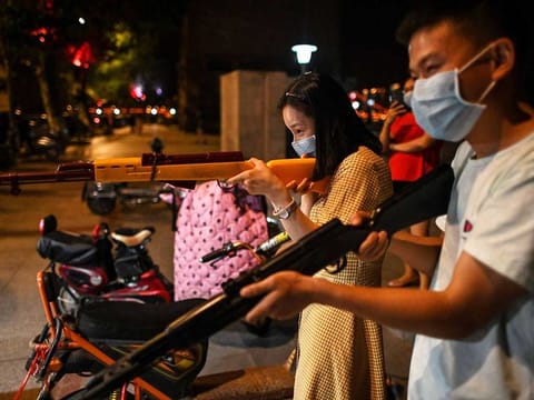 A couple tries to burst balloons with toy guns at a night stall along the Yangtze River in Wuhan in China’s central Hubei province on May 19, 2020. 