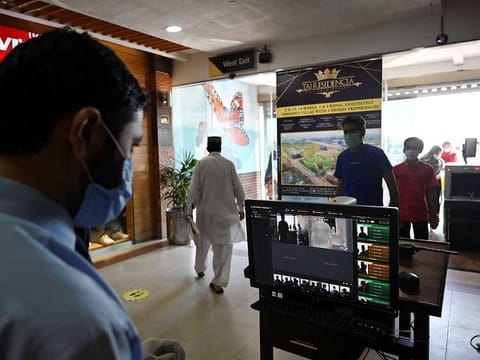 In this picture taken on May 18, 2020 a shopping mall official (L) uses thermal scanner to check the temperature of shoppers before they enter at the Centaurus Mall after the government eased a nationwide lockdown imposed as a preventive measure against the COVID-19 coronavirus, in Islamabad.  Pakistan's intelligence agencies are using secretive surveillance technology they initially deployed to locate militants to instead track people who have tested positive for the new coronavirus, officials told AFP.