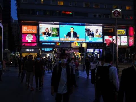Pedestrians pass a screen showing a news broadcast of Chinese Premier Li Keqiang attending the National People’s Congress in Beijing, at night in Hong Kong, China, on Thursday, May 28, 2020. 