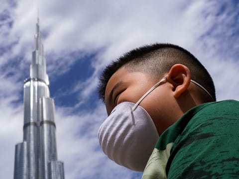A boy wearing mask walks through a street near Burj Khalifa.