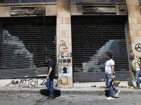 Lebanese men pass next of a shop that was damaged by angry protesters, during an anti-government protest, in Beirut, on June 12, 2020. 