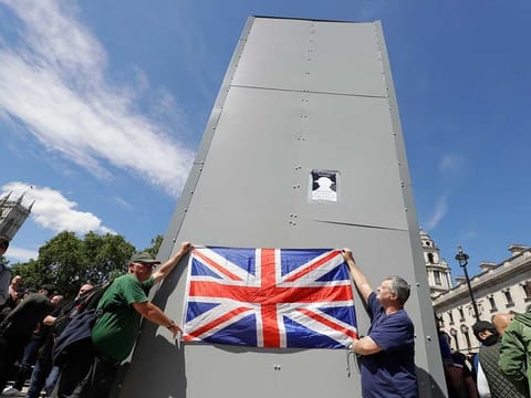 Members of far-right Football Lads Alliance hold a British flag in front of a protective covering surrounding the statue of former British Prime Minister Sir Winston Churchill in Parliament Square, central London, Saturday, June 13, 2020. British police have imposed strict restrictions on groups planning to protest in London Saturday in a bid to avoid violent clashes between protesters from the Black Lives Matter movement, as well as far-right groups.