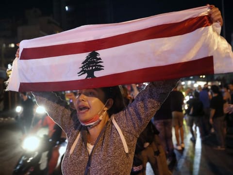 An anti-government protester chants slogans as she holds up a Lebanese flag joining others to block a road during a protest against the political leadership they blame for the economic and financial crisis, in Beirut on June 11.