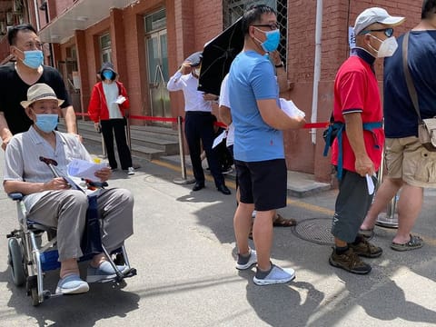 A man is pushed past a line of residents waiting to be tested at a fever clinic in Beijing on Monday, June 15, 2020. 
