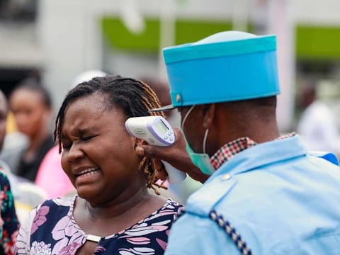 A security guard uses a thermal scanner to check a woman's temperature as she enters the Tejuoso shopping complex at the Yaba market, amid the coronavirus disease (COVID-19) outbreak, in Lagos, Nigeria March 23, 2020. 
