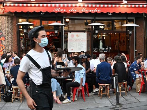 A waiter wearing a face mask serves clients while people eat and have drinks on the terrace of the cafe-restaurant "Le Bar du Marche"  in Paris as cafes and restaurants reopen in France with the easing of lockdown mesures taken to curb the spread of the COVID-19 pandemic, caused by the novel coronavirus.