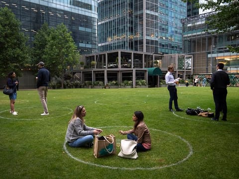People stand within rings marked on the grass to maintain their social distance outside a bar in Canary Wharf, East London as further coronavirus lockdown restrictions are lifted in England, on Wednesday, July 1, 2020.