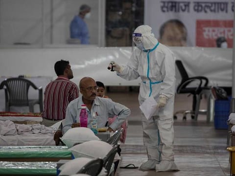 A health official wearing Personal Protective Equipment (PPE) suit talks to patients inside the campus hall of spiritual organisation Radha Soami Satsang Beas (RSSB), converted into a COVID-19 coronavirus care centre in New Delhi on July 6, 2020. 
