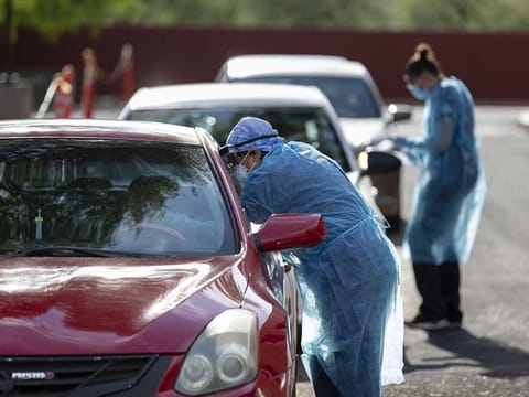 Healthcare workers wearing personal protective equipment (PPE) administer tests at an El Rio Health COVID-19 drive-through testing site in Tucson, Arizona, U.S., on Monday, July 13, 2020. 