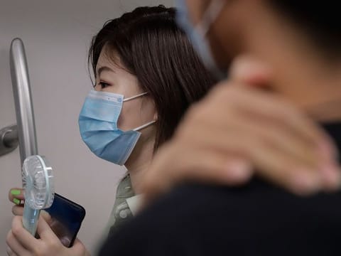 A woman wearing a face mask to protect against the new coronavirus uses an electric fan to cool herself as she rides in a subway train in Beijing, Wednesday, July 29, 2020.