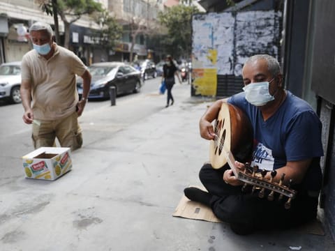 A street musician man performs with a mask on his face to help stop the spread of the coronavirus, as other man on the left puts money on a box, in Beirut, Lebanon, Wednesday, July 29, 2020.  Lebanon is hurtling toward a tipping point at an alarming speed, driven by financial ruin, collapsing institutions, hyperinflation and rapidly rising poverty _ with a pandemic on top of that. The collapse threatens to break a nation seen as a model of diversity and resilience in the Arab world.