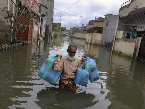 A man carries goods as he wades through a flooded street after heavy monsoon rains, in Karachi, Pakistan, Wednesday, Aug. 26, 2020. 
