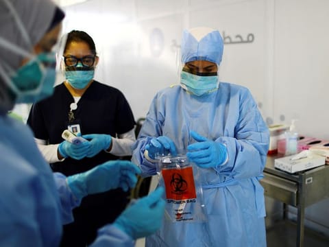 A member of medical staff wearing a protective face mask and gloves carries a swab tested during drive-through coronavirus disease testing (COVID-19) at a screening centre in Abu Dhabi