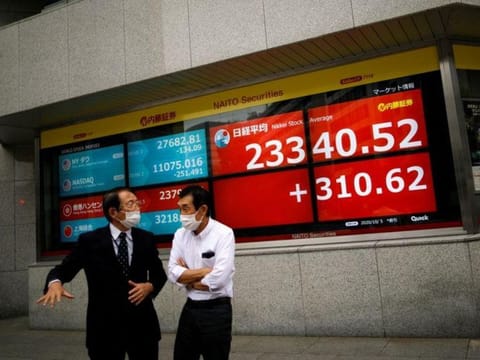 Men wearing protective face masks chat in front of a screen displaying Nikkei share average and world stock indexes outside a brokerage, amid the coronavirus disease (COVID-19) outbreak, in Tokyo, Japan October 5, 2020. 