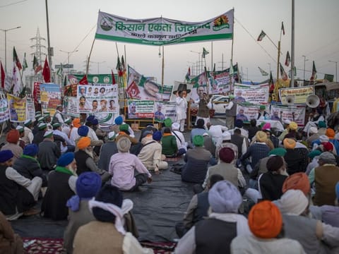 Farmers listen to a speaker, sitting in the middle of an expressway at the site of a protest against new farm laws at the Delhi-Uttar Pradesh state border, India, Wednesday, December 9, 2020.  