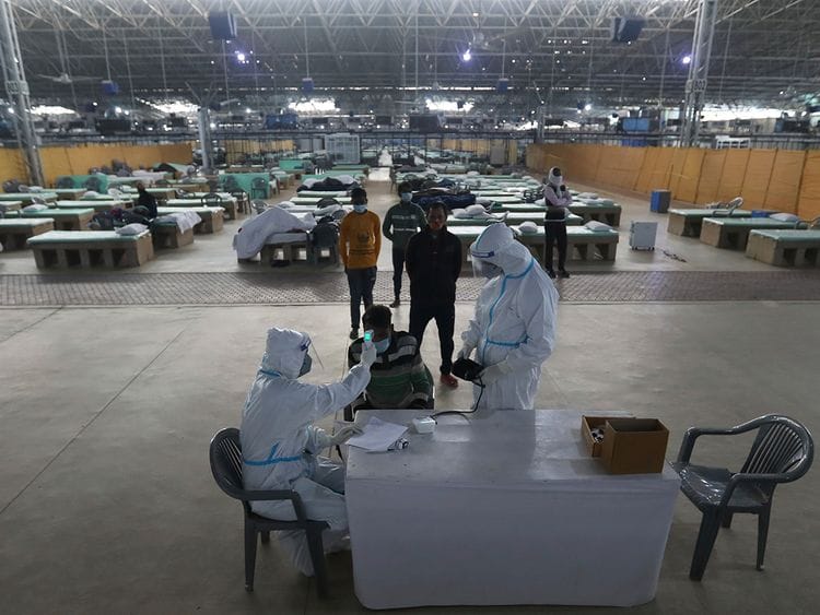 Health workers check the body temperature of patients recovering at the Sardar Patel Covid Care Center hospital after getting, in New Delhi. 