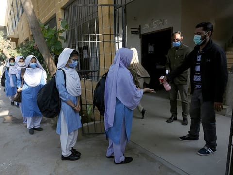 A worker sprays sanitizer on the hands of students wearing face masks to prevent the spread of the coronavirus as they arrive at their school, in Karachi, Pakistan, Monday, Jan. 18, 2021. 