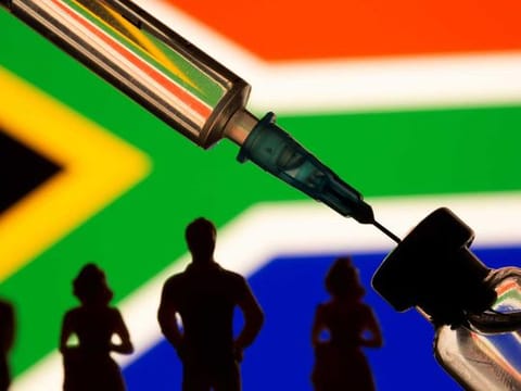 A vial, syringe and small toy figures are seen in front of displayed South Africa flag in this illustration 