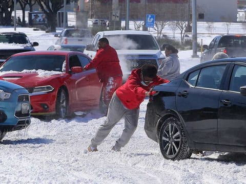 People push a car free after spinning out in the snow Monday, Feb. 15, 2021 in Waco, Texas. A winter storm that brought snow, ice and plunging temperatures across the southern Plains and caused a power emergency in Texas stretched its frigid fingers down to the Gulf Coast. 