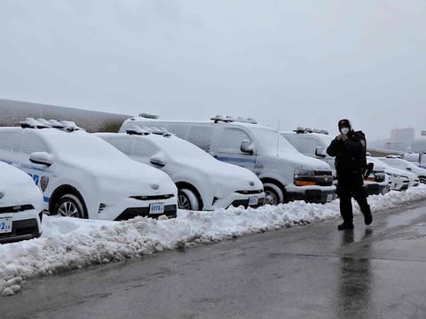 An officer from the New York Police Department (NYPD) walks by a row of police vehicles buried in snow near the Hudson Yards precinct in Manhattan, New York City 