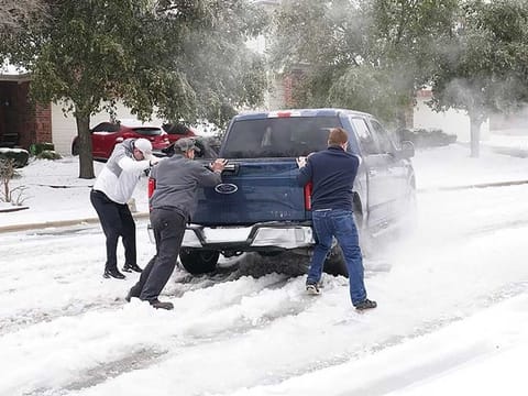Residents help a pickup driver get out of ice on the road in Round Rock, Texas, on February 17, 2021, after a winter storm. 