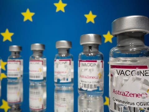Vials labelled with partially torn sticker "AstraZeneca COVID-19 Coronavirus Vaccine" are seen in front of a displayed EU flag in this illustration.