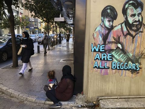 People pass next of a woman, centre, who is sits on the ground with her daughter begging on Beirut's commercial Hamra Street on March 16, 2021. More than half the population now lives in poverty, while an intractable political crisis heralds further collapse and Lebanese are gripped by fear for the future. 