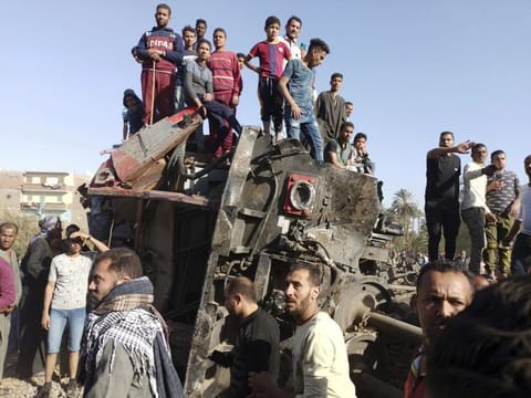 Egyptians gather around mangled train carriages at the scene of a train accident in Sohag, Egypt, Friday, March 26, 2021.  