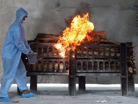 A frontline worker in personal protective equipment (PPE) sprays a flammable liquid on a burning funeral pyre of a man who died from COVID-19, at a crematorium on the outskirts of Mumbai. 