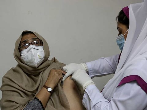 A woman reacts while receiving the second shot of the Sinopharm COVID-19 vaccine from a health worker at a vaccination centre, in Peshawar, Pakistan, Wednesday, April 21, 2021. 