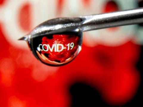 The word "COVID-19" is reflected in a drop on a syringe needle in this illustration. 