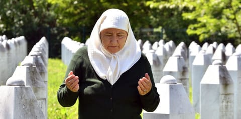 A picture taken on May 26, 2021, shows Bosnian Muslim woman Fadila Efendic, 69, survivor of 1995 Srebrenica massacre, as she prays near tombstones of her husband and son during her visit to the Memorial cemetery in Potocari-Srebrenica set up to honour the victims of the 1995 Srebrenica massacre. Bosnian Serb wartime military chief Ratko Mladic currently awaits the final verdict upon his appeal. 