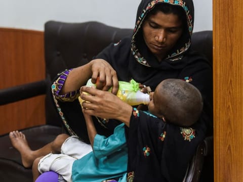 In this picture taken on March 25, 2021, a mother feeds her HIV positive son while waiting for their turn at an HIV treatment support centre in Rato Dero, in southern Sindh province. 