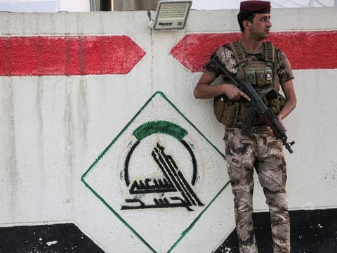 In this file photo taken on June 13, a fighter of Iraq's Hashd Al Shaabi (Popular Mobilisation Units) paramilitary forces stands guard next to a wall showing the group's logo outside their headquarters in Baghdad. 